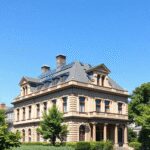 Rénovation patrimoniale et performance énergétique : concilier histoire et durabilité en secteur protégé Bâtiment historique avec une architecture classique et des panneaux solaires modernes sur le toit, entouré de verdure sous un ciel bleu clair.